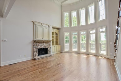 Unfurnished living room featuring a towering ceiling, ornamental molding, light wood-style floors, baseboards, and a stone fireplace