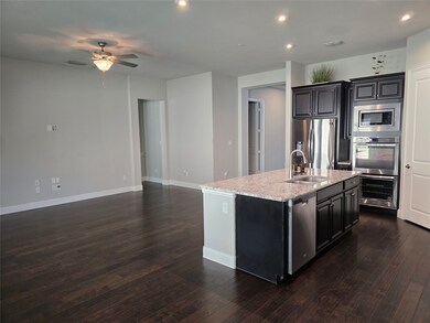 Kitchen featuring dark cabinetry, an island with sink, open floor plan, dark wood-type flooring, and stainless steel appliances