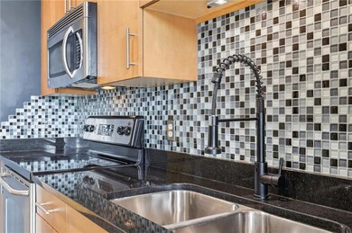 Kitchen with appliances with stainless steel finishes, backsplash, a sink, dark stone countertops, and light brown cabinetry