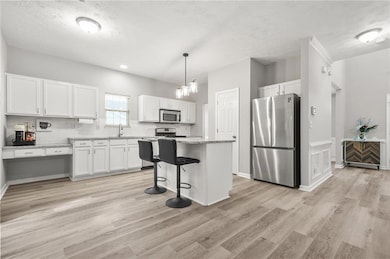 Kitchen with stainless steel appliances, white cabinets, light wood-type flooring, and a kitchen island