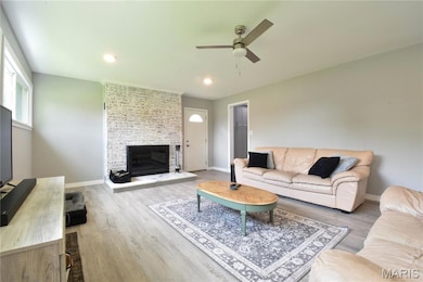 Living room with a ceiling fan, wood finished floors, a stone fireplace, and recessed lighting