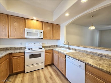 Kitchen with white appliances, recessed lighting, light wood-style floors, pendant lighting, and brown cabinetry