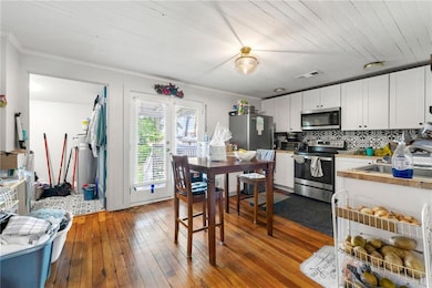Kitchen featuring stainless steel appliances, decorative backsplash, wood-type flooring, white cabinetry, and ornamental molding