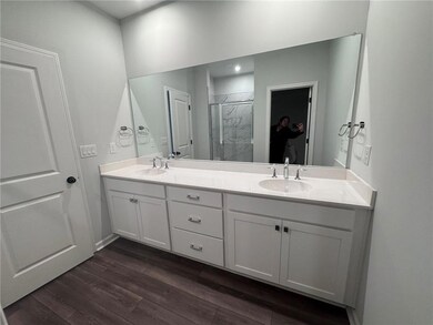 Bathroom with double vanity, a marble finish shower, and dark wood-style flooring