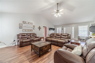 Living area featuring light wood-style flooring, a ceiling fan, healthy amount of natural light, baseboards, and high vaulted ceiling