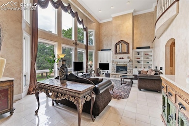 Living room featuring a towering ceiling, light tile patterned flooring, crown molding, a fireplace, and arched walkways