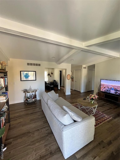 Living room featuring beamed ceiling and dark wood-style flooring