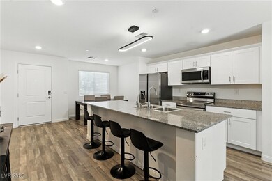 Kitchen with appliances with stainless steel finishes, a kitchen breakfast bar, a kitchen island with sink, white cabinets, and wood finished floors