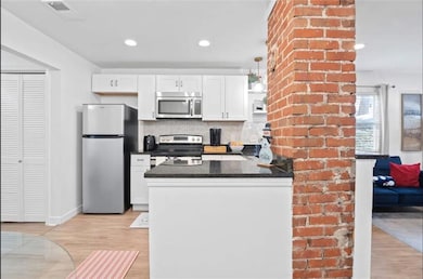 Kitchen featuring stainless steel appliances, a peninsula, white cabinetry, backsplash, and recessed lighting