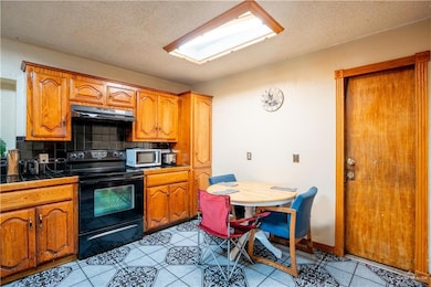 Kitchen with electric range, brown cabinets, decorative backsplash, tile counters, and a textured ceiling