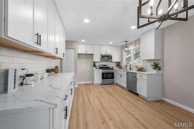 Kitchen with white cabinets, light stone counters, appliances with stainless steel finishes, a chandelier, and recessed lighting