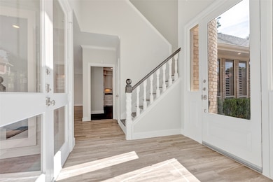 Bright and inviting entryway featuring large windows, a glass door, and elegant wood flooring. A staircase with white balusters leads to the upper level, and there’s a view of a cozy interior space.