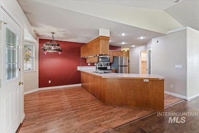 Kitchen with light countertops, vaulted ceiling, light wood finished floors, brown cabinets, and a chandelier