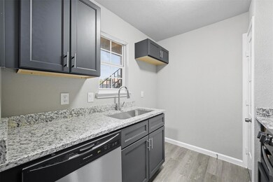 Kitchen with light wood-style flooring, dishwasher, light stone counters, gray cabinets, and range