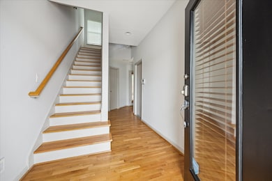 You are greeted by a bright entryway with wood flooring, a sleek staircase, and ample natural light from a window at the top landing.
