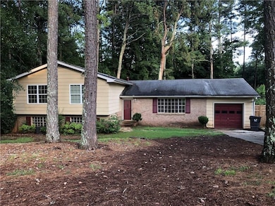 Split level home with a garage, brick siding, driveway, and view of scattered trees