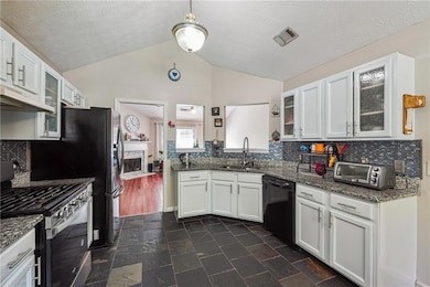 Kitchen with stainless steel gas range oven, dishwasher, lofted ceiling, under cabinet range hood, and white cabinetry