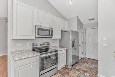 Kitchen with stainless steel appliances, visible vents, white cabinetry, and vaulted ceiling