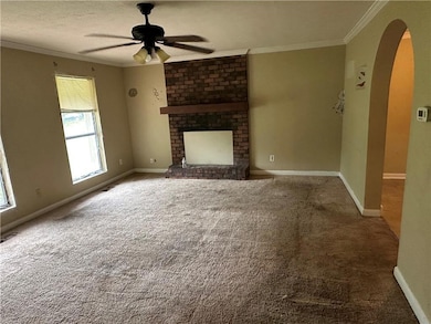 Unfurnished living room featuring arched walkways, crown molding, a ceiling fan, carpet flooring, and a fireplace