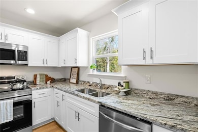 Kitchen with white cabinetry, appliances with stai