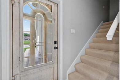 This photo showcases the entryway of a home, featuring a glass-paneled front door and a staircase with carpeted steps leading to the upper floor. Natural light brightens the space, highlighting the neutral wall colors.