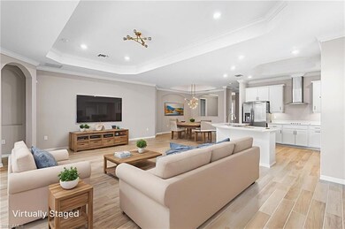 Living area featuring a tray ceiling, crown molding, light wood-style floors, recessed lighting, and a chandelier