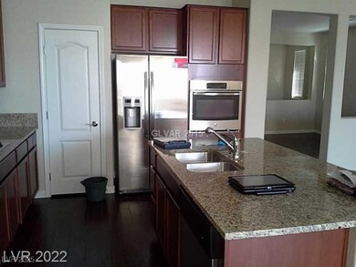 Kitchen with appliances with stainless steel finishes, light stone countertops, a center island with sink, dark wood-style flooring, and dark brown cabinets