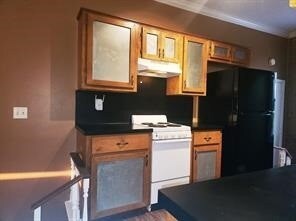 Kitchen with dark countertops, white range, freestanding refrigerator, under cabinet range hood, and crown molding