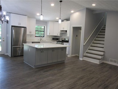 Kitchen featuring appliances with stainless steel finishes, a kitchen island, white cabinetry, under cabinet range hood, and dark wood-style floors