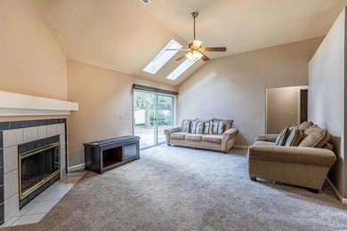 Living area with light carpet, high vaulted ceiling, a ceiling fan, baseboards, and a tile fireplace