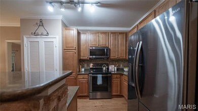Kitchen featuring stainless steel appliances, ornamental molding, decorative backsplash, light wood-style floors, and brown cabinets