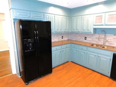 Kitchen featuring black fridge, blue cabinetry, tasteful backsplash, and light wood finished floors