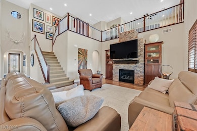 Living area featuring arched walkways, a towering ceiling, wood finished floors, a stone fireplace, and healthy amount of natural light