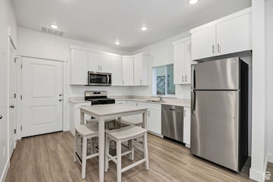 Kitchen with stainless steel appliances, light wood-style floors, white cabinetry, and recessed lighting
