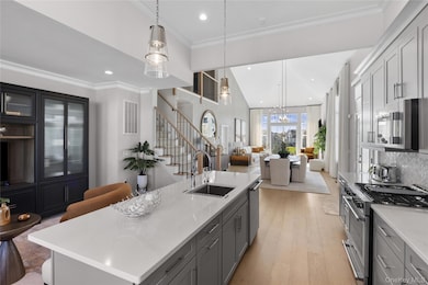 Kitchen with gray cabinets, crown molding, stainless steel appliances, a kitchen island with sink, and open floor plan