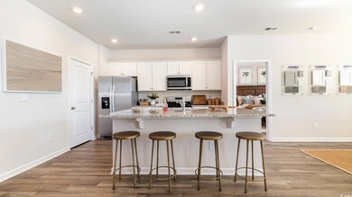 Kitchen featuring appliances with stainless steel finishes, a breakfast bar area, white cabinets, an island with sink, and light stone countertops