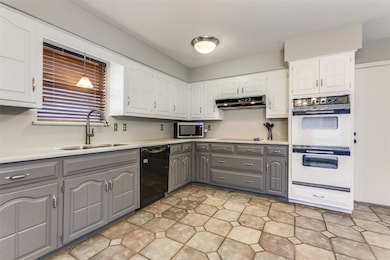 Kitchen with gray cabinets, light countertops, double oven, and white cabinets