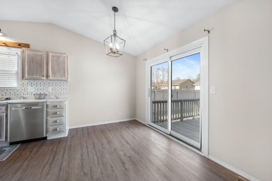 Kitchen featuring dark wood-style floors, backsplash, vaulted ceiling, dishwasher, and pendant lighting