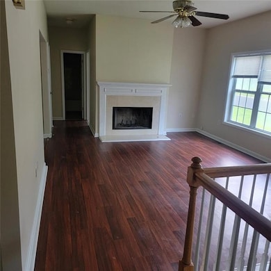 Unfurnished living room featuring ceiling fan, dark wood finished floors, and a premium fireplace