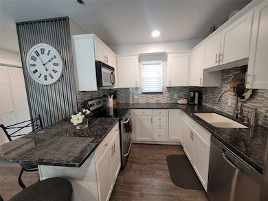 Kitchen featuring white cabinetry, a kitchen bar, stainless steel appliances, dark stone counters, and sink