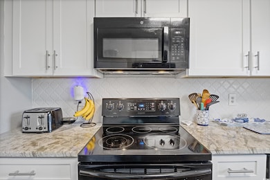 Kitchen with black appliances, white cabinets, backsplash, and light stone counters