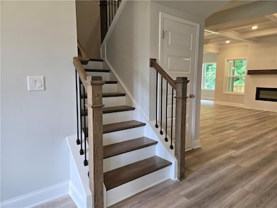 Stairs with wood finished floors, baseboards, coffered ceiling, beamed ceiling, and a glass covered fireplace