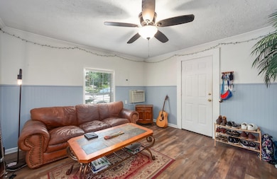 Living area with a wainscoted wall, a textured ceiling, wood finished floors, a ceiling fan, and ornamental molding