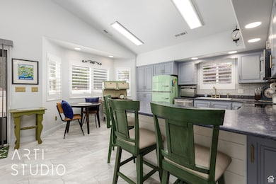 Kitchen with freestanding refrigerator, dark countertops, gray cabinetry, lofted ceiling, and decorative backsplash