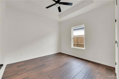 Unfurnished room with dark wood-type flooring, a raised ceiling, a ceiling fan, and baseboards