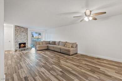 Living room with light wood finished floors, a stone fireplace, and a ceiling fan