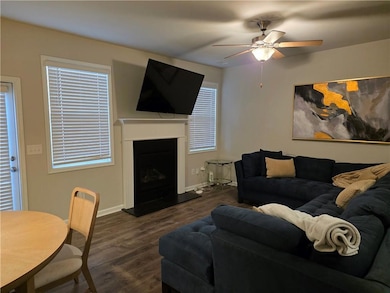 Living area with dark wood-style flooring, a fireplace with raised hearth, and ceiling fan
