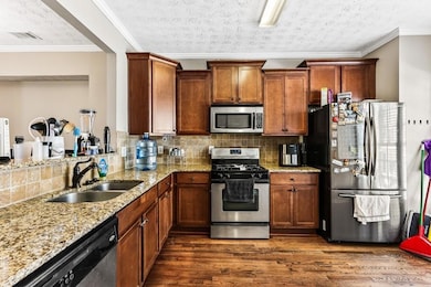 Kitchen featuring decorative backsplash, appliances with stainless steel finishes, crown molding, dark wood finished floors, and light stone counters