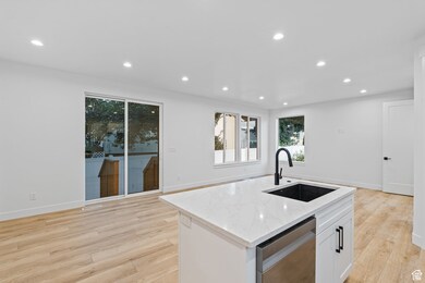 Kitchen with recessed lighting, light stone counters, white cabinetry, stainless steel dishwasher, and a kitchen island with sink