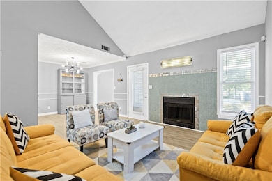 Living room featuring a tiled fireplace, high vaulted ceiling, a chandelier, wood finished floors, and crown molding